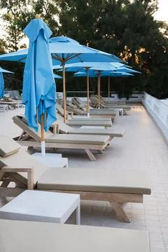 Empty sun lounge chairs with blue umbrellas near the pool in hotel tourist re Stock Photos