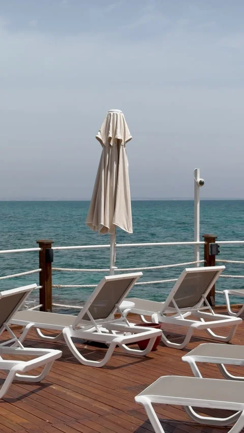 Empty sunbeds and closed beach umbrella on wooden pier by the sea, luxury resort Stock Footage 346307442