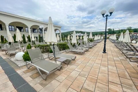 Empty sunbeds and umbrellas on pool terrace at spa resort exterior on cloud.. Stock Photos