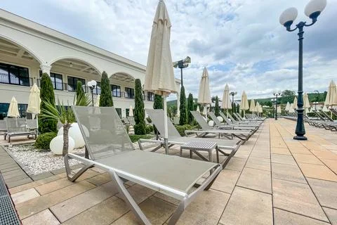 Empty sunbeds and umbrellas on pool terrace at spa resort exterior on cloud.. Stock Photos
