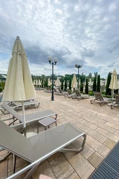 Empty sunbeds and umbrellas on pool terrace at spa resort exterior on cloud.. Stock Photos