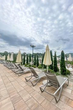 Empty sunbeds and umbrellas on pool terrace at spa resort exterior on cloud.. 库存照片