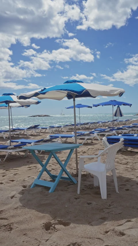 Empty sunbeds under blue umbrellas on a sandy beach with a clear sky and se.. Stock Footage 276949025