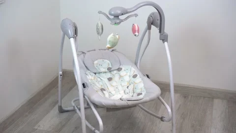 An empty swing-cradle swings in the room. Children's automatic swing for an Video stock 220732459