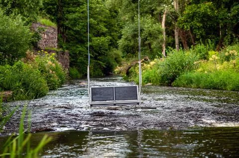 Empty swing hanging on ropes above a fast flowing river, concept of active re Stock Photos