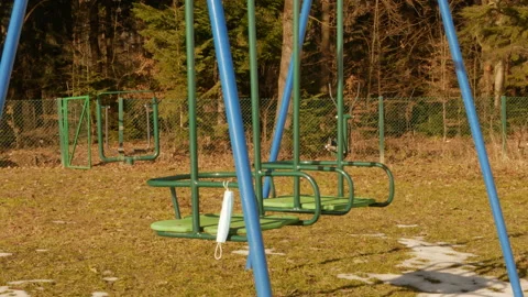 Empty swing on a playground during quarantine. surgical mask waves on a wind Stock Footage 150557166