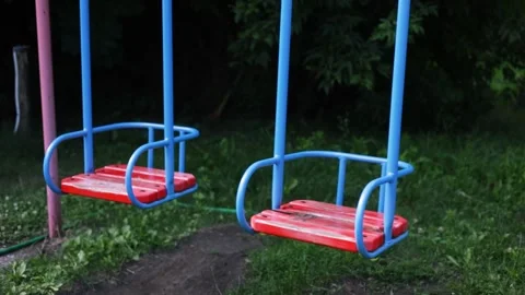 Empty swing seat gently moving on a peaceful green playground Stock Footage 340519432