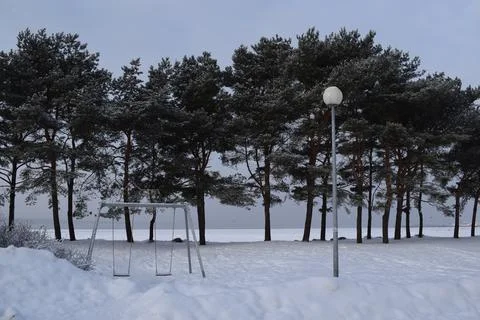 An empty swing set and a round street lamp standing in deep white snow Stock Photos