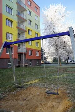 Empty swing set in front of colorful apartment building on frosty winter mo.. Stock Photos