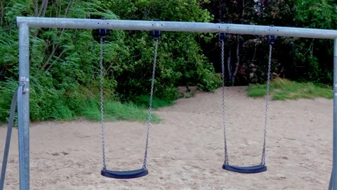Empty swing set on sandy beach playground surrounded by green coastal trees Stock Footage 344356020