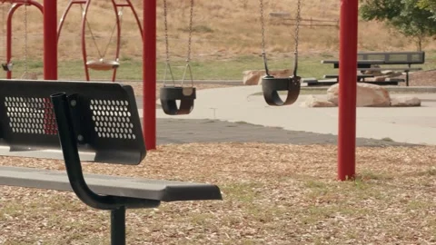 Empty Swing Set Swaying Behind Foreground Park Bench Video stock 345540770