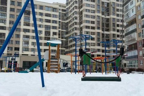Empty swing on a snowy playground in front of a modern residential building.. Stock Photos
