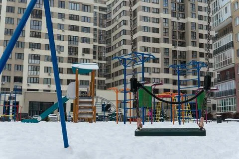 Empty swing on a snowy playground in front of a modern residential building.. Stock Photos