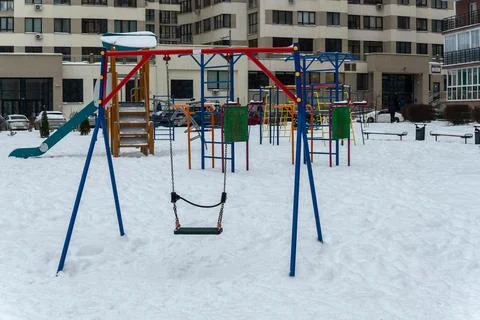 Empty swing on a snowy playground in winter. Lonely swing seat hanging on c.. Stock Photos
