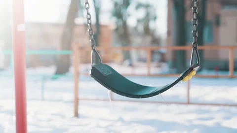 Empty Swing Swinging on Chain at Snowy Playground on Sunny Winter Day Stock Footage 329655072