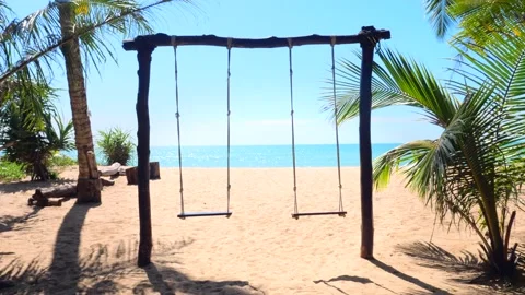 Empty swing swinging on a sandy tropical beach with turquoise sea and green palm Stock Footage 199362738