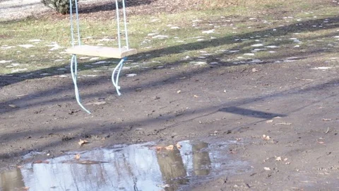 Empty swing, swinging in the wind after spring rain over a puddle of water. Stock Footage 102625874
