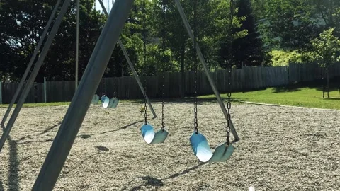 Empty swings moving slowly on playground in summer park at daytime. Stock Footage 337625860