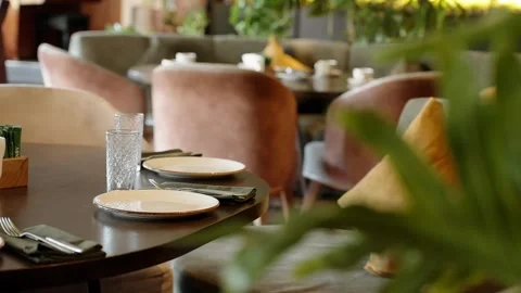 Empty table set for dinner with plates and glasses in restaurant with greenery Stock Footage 327390450