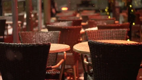 Empty tables and chairs of outdoor cafe on snowy street in evening. Stock Footage 335516955