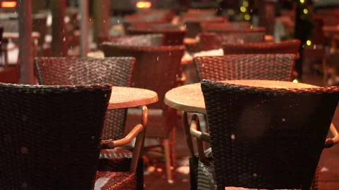 Empty tables and chairs of outdoor cafe on snowy street in evening. Stock Footage 335517088