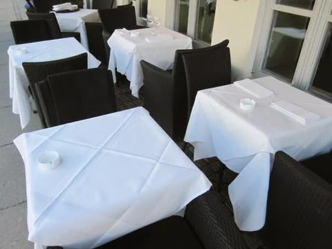 Empty tables covered in white cloths outside restaurant and cafe Stock Photos