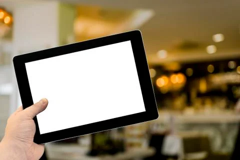 Empty tablet PC in hand in cafe bar interior with lamps Stock Photos