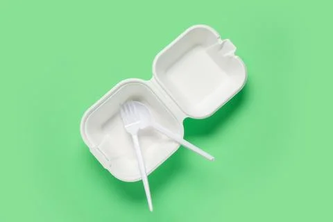 Empty takeaway food container with plastic cutlery on green background Stock Photos