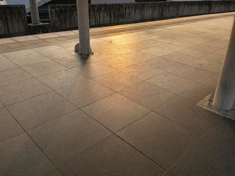 Empty train station platform floor bathed in warm golden hour sunlight Stock Photos
