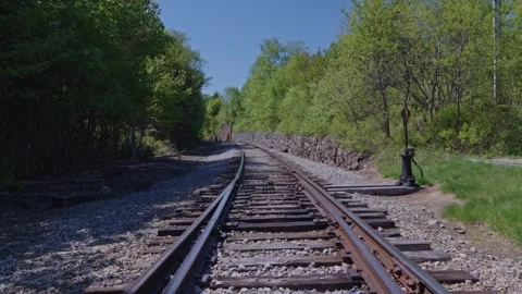Empty train tracks curving past stone wall and switch stand into green and Stock Footage 337536446