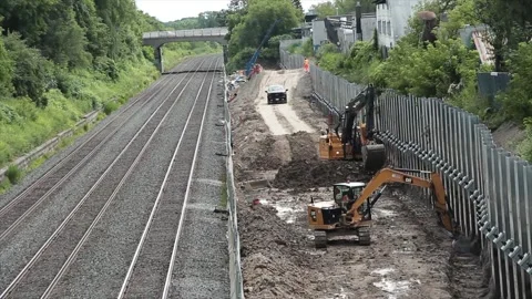 Empty train tracks with train passing with construction equipment to right Stock Footage 247753692