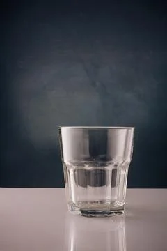 Empty transparent glass on white table, dark backdrop. Glassware Stock Photos