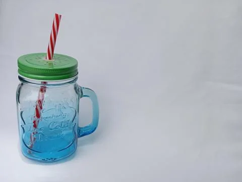 Empty transparent mason jar with a handle, red straw and green lid on white Stock Photos