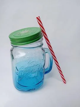 Empty transparent mason jar with a handle, red straw and green lid on white Stock Photos
