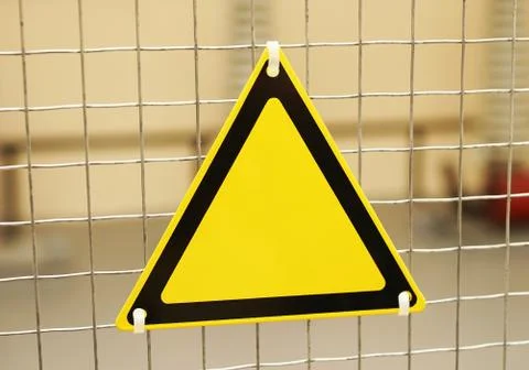 Empty triangular yellow sign on a mesh fence. Stock Photos
