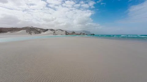 Empty turquoise beach beneath dunes and clouds Stock Photos