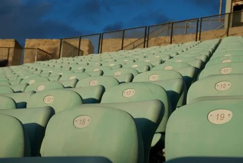 Empty turquoise stadium seats in rows under warm golden-hour light. Stock Photos