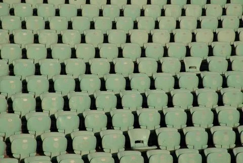 Empty turquoise stadium seats in rows under warm golden-hour light. Stock Photos