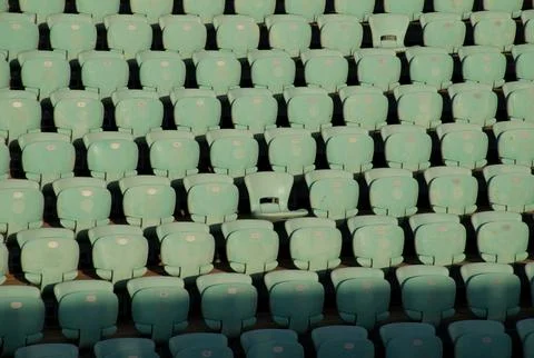 Empty turquoise stadium seats in rows under warm golden-hour light. Stock Photos