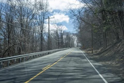 Empty Two Lane Road Through Leafless Forest Under Blue Sky Stock Photos