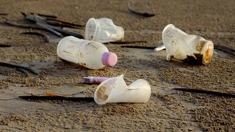 Empty used dirty plastic bottles and cups trash lying on the sea beach Stock Photos