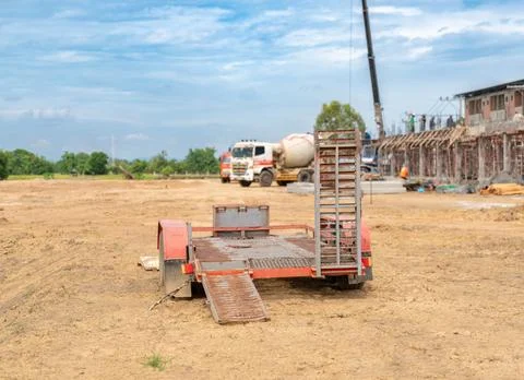An empty utility trailer with loading ramps parked on a dirt ground at a co.. 스톡 사진