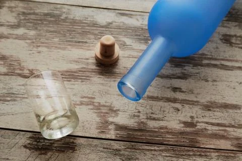 Empty vodka bottle on the table next to a shot glass and cork, alcohol proble Stock Photos