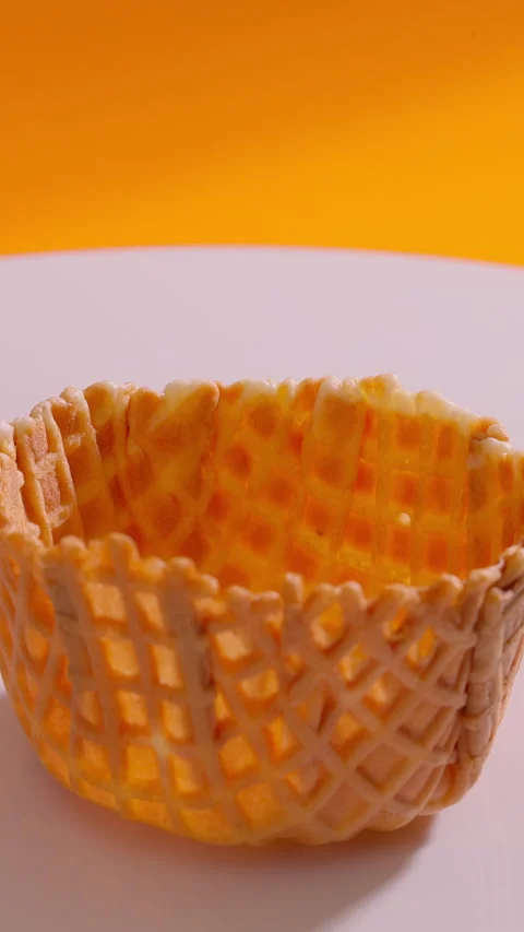 Empty waffle cone rotating against orange background. Vertical close-up shot Stock Footage 313159529