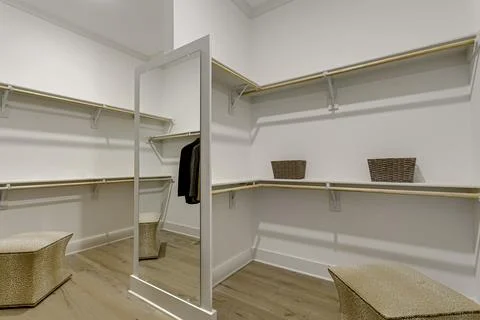 Empty Walk-In Closet With Shelving, Mirror, And Ottoman On Wooden Floor. Stock Photos