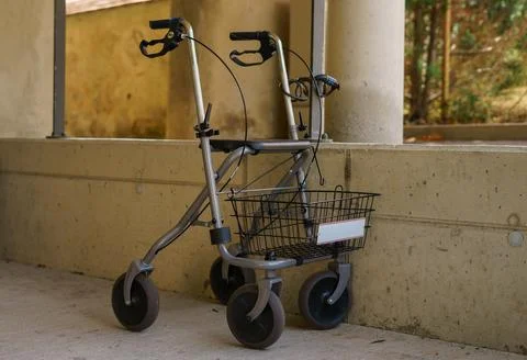 Empty walker for elderly with basket parked against concrete wall outdoors Stock Photos