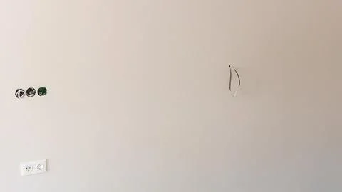 Empty wall with electrical outlets and a single hanging wire, showcasing a .. Stock Photos