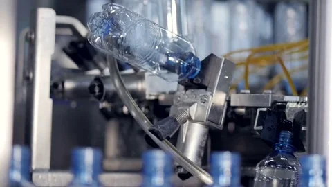 Empty water bottles grabbed from a conveyor line by a cleaning rotary wheel. 4K. Stock-Footage 77379640