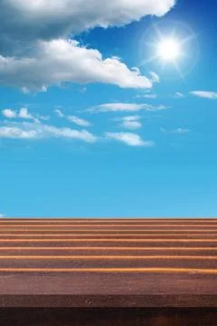 Empty weathered table top against a bright blue sky with white clouds and s.. Stock Photos