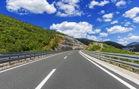 An empty, well-maintained asphalt road winding through a sunny, mountainous Foto stock